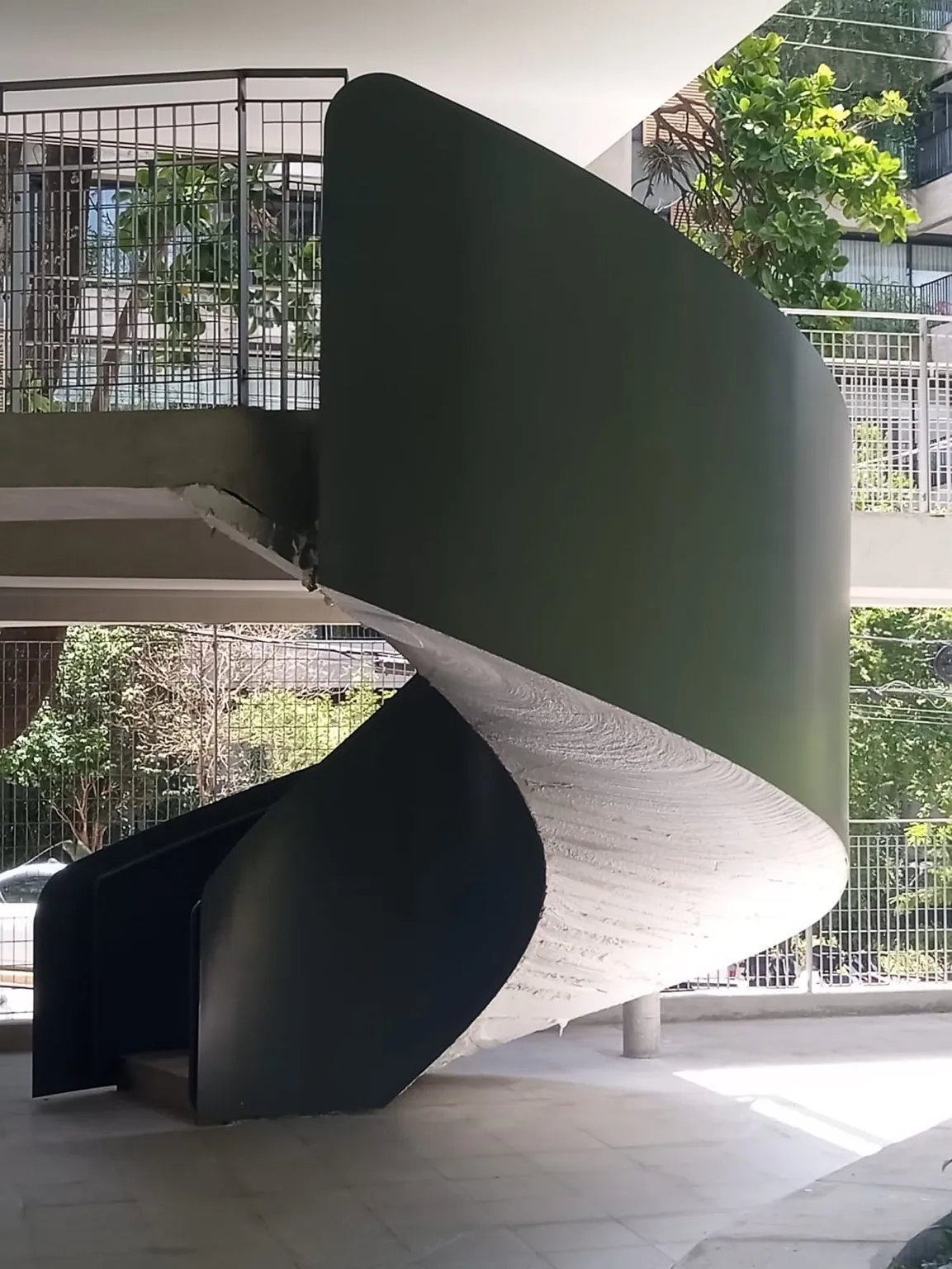 Escada helicoidal de desenho escultórico com guarda-corpo metálico preto