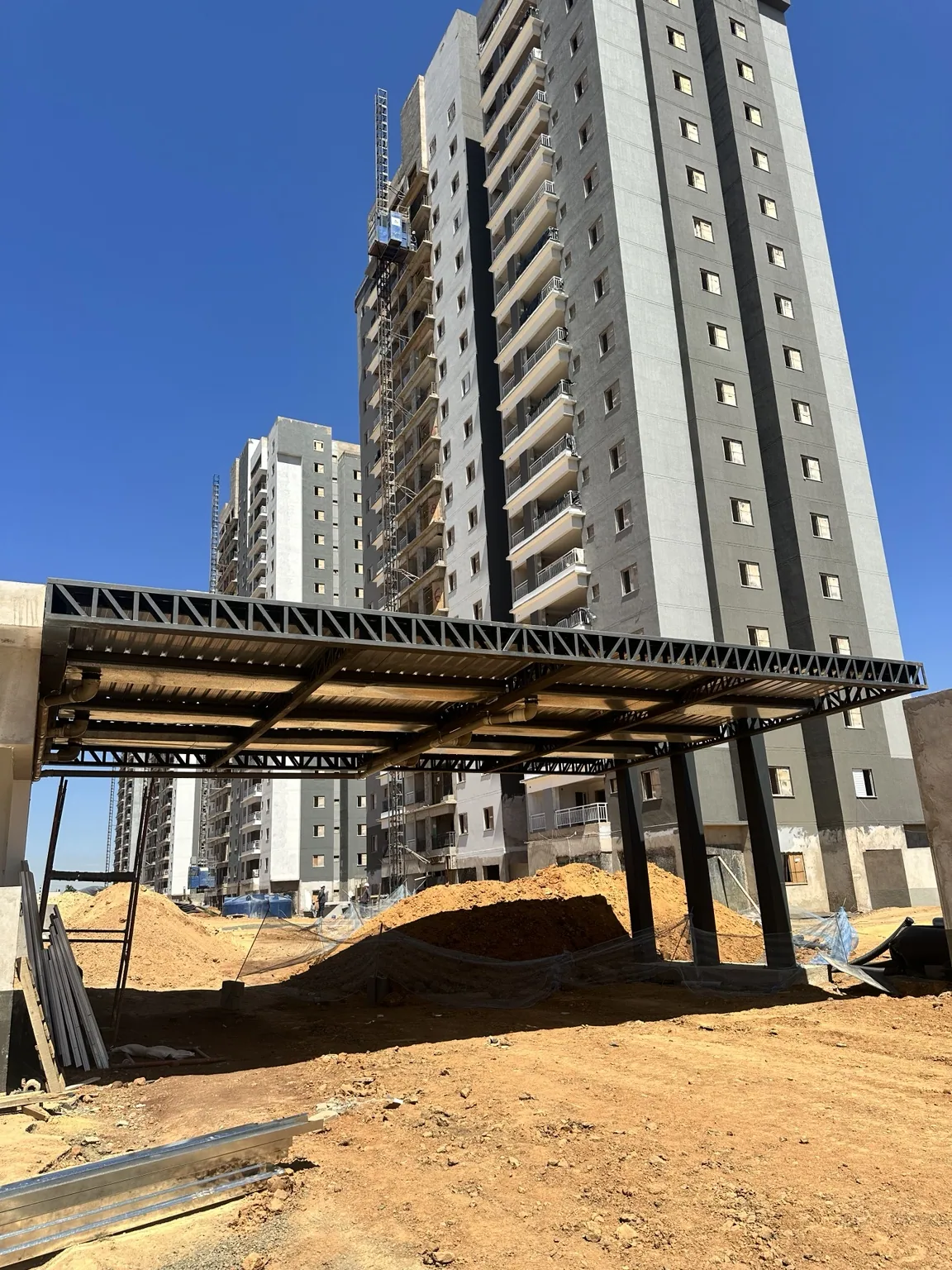 Cobertura metálica treliçada junto a edifício residencial em construção