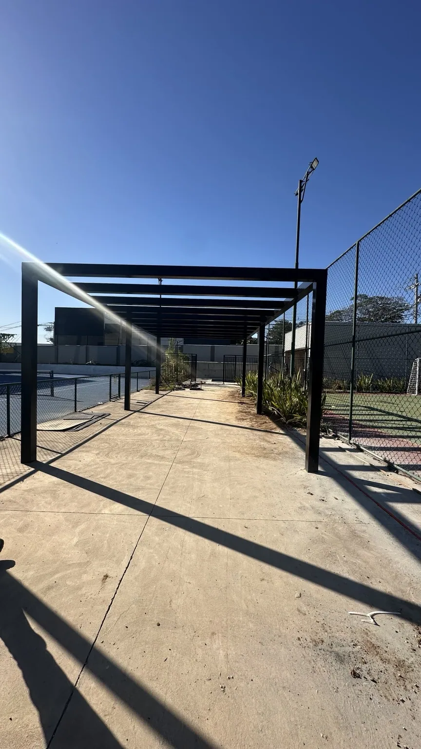 Pergolado de aço preto sobre passagem externa junto a área esportiva